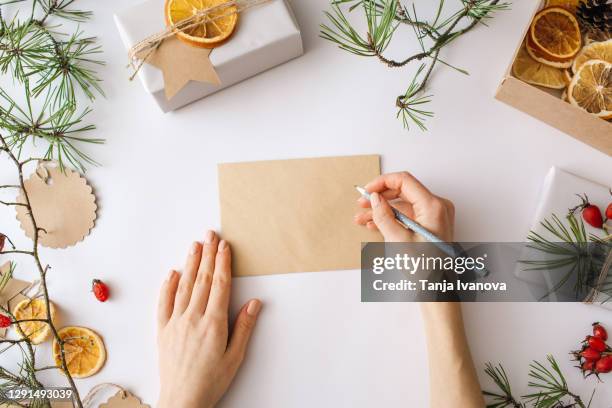 christmas blank greeting card mock-up. woman writing in a blank letter festive winter composition. craft envelope, gift boxes, nature decorations on white background. flat lay, top view, copy space. - copy writing bildbanksfoton och bilder