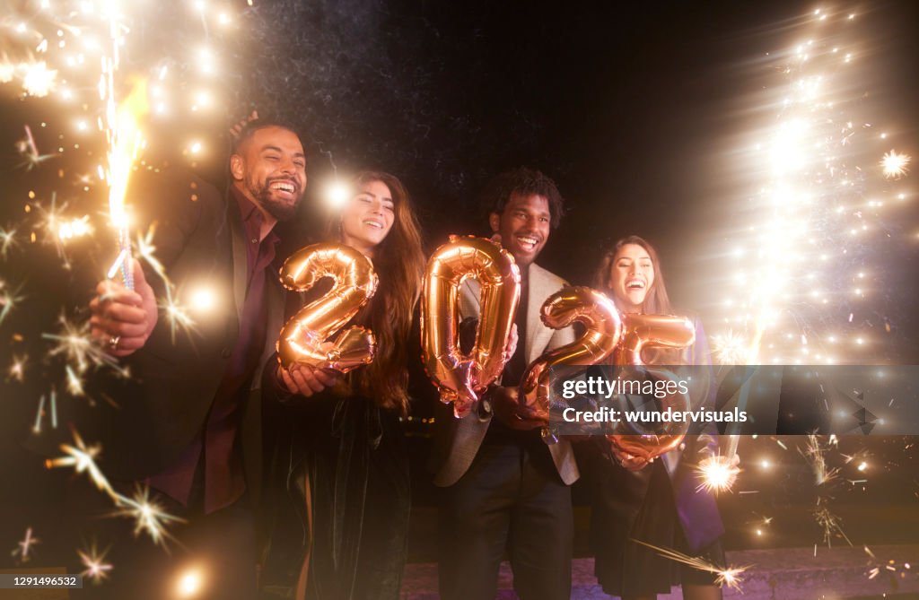 Gruppo di amici che festeggiano i nuovi anni tenendo palloncini e scintille 2025