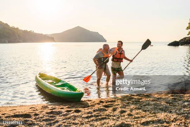 male kayakers walking onto beach with paddles after exercise - life jacket isolated stock pictures, royalty-free photos & images