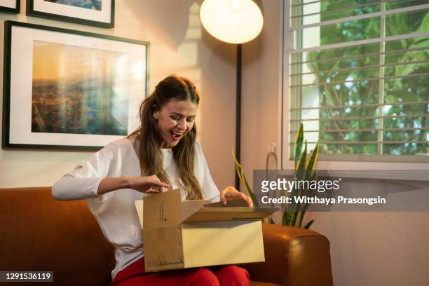 happy young woman customer open parcel box sit on sofa - geschenk auspacken stock-fotos und bilder