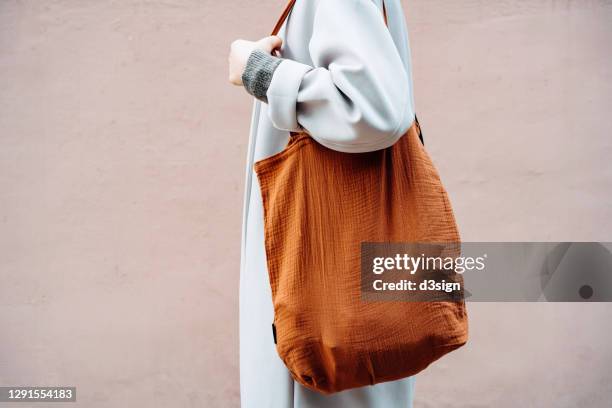 cropped shot and mid section of young asian woman carrying a brown reusable bag shopping in the city, standing against a pink wall in background. responsible shopping, zero waste, sustainable lifestyle concept - herbruikbare tas stockfoto's en -beelden