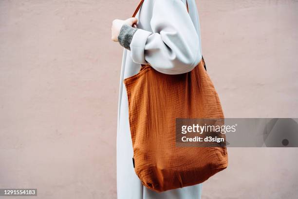 cropped shot and mid section of young asian woman carrying a brown reusable bag shopping in the city, standing against a pink wall in background. responsible shopping, zero waste, sustainable lifestyle concept - carrying on shoulders stock pictures, royalty-free photos & images