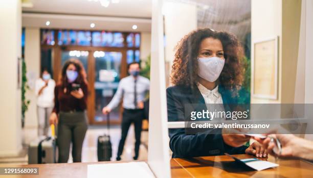hotelgäste mit schützenden gesichtsmasken und sozialer entsagung vor der hotelrezeption - gast stock-fotos und bilder