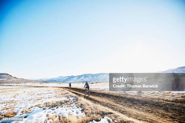 friends descending hill on gravel bikes while riding through snowy landscape on winter afternoon - winter cycling ストックフォトと画像