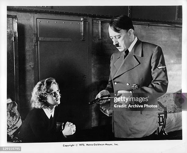 Alec Guinness looking at a gun as an unknown actress looks up at him in a scene from the film 'Hitler: The Last Ten Days', 1973.