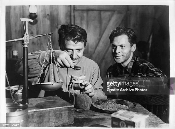 John Agar watches unknown actor measure the gold in a scene from the film 'Hold Back Tomorrow', 1955.