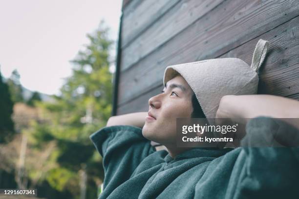 young man enjoying sauna wearing sauna hat - sauna stock pictures, royalty-free photos & images