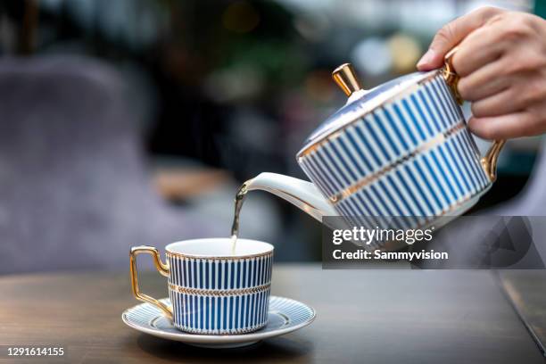 pouring black tea into cup - theepot stockfoto's en -beelden