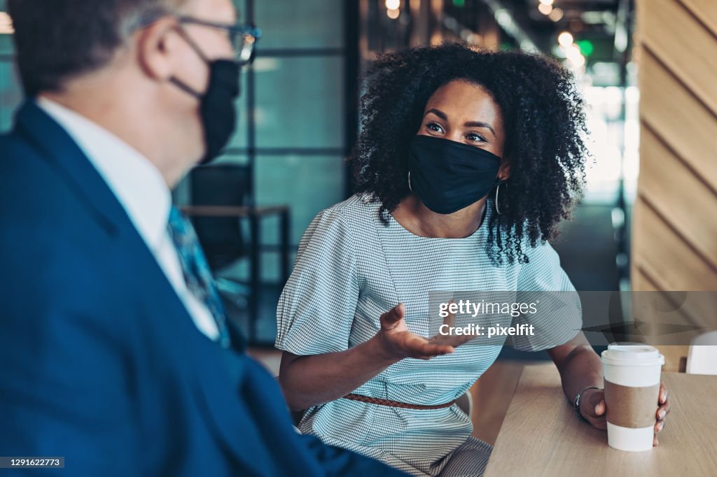 Businesswoman and businessman with masks talking in the office