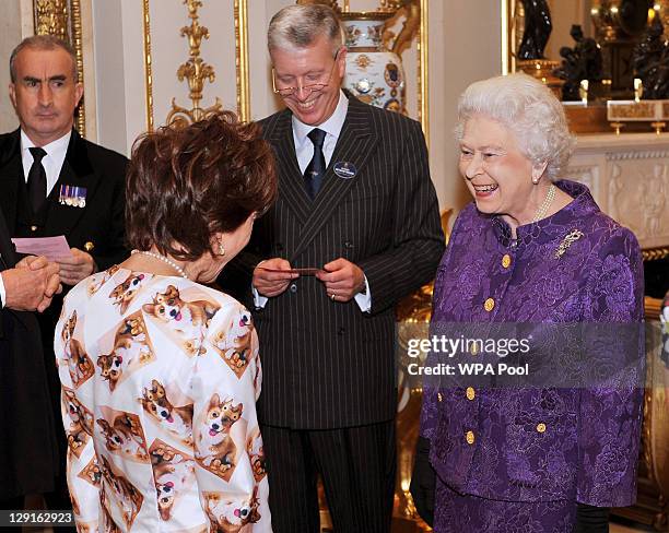 Queen Elizabeth II talks with Kathy Lette, wearing an outfit decorated in corgis wearing crowns, in the white drawing room at Buckingham Palace,...