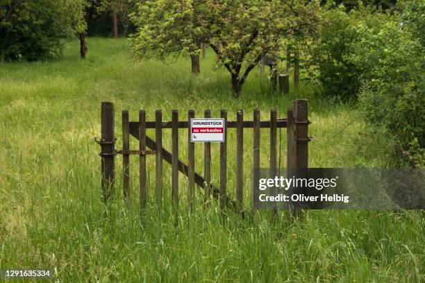 a single segment of a fence stands in the middle of a green meadow with tree. attached to it is a sign with the inscription "land for sale" and a blank space for the phone number - grounds stock-fotos und bilder