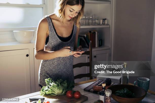 young woman looking at recipe on smart phone at home - woman cooking phone stock-fotos und bilder