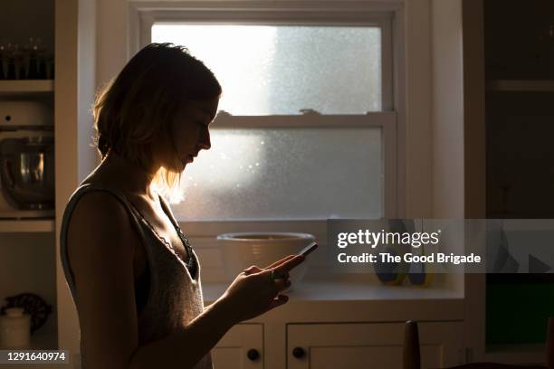 silhouette of young woman looking at smart phone - dark background light stock-fotos und bilder
