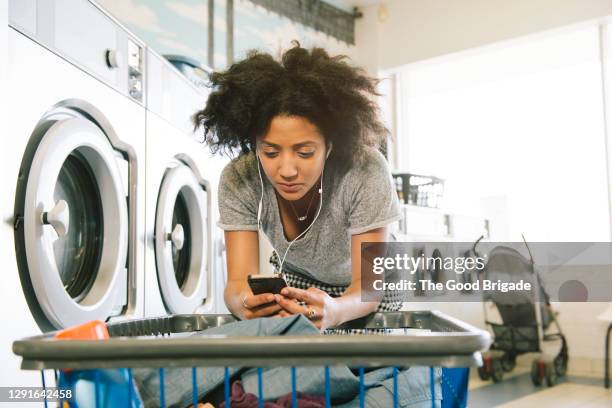 young woman listening to headphones in laundromat - waschsalon stock-fotos und bilder