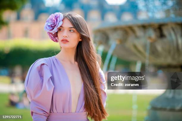 joven con vestido morado y fascinador de flores junto a la fuente - fascinator fotografías e imágenes de stock