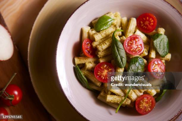 bowl of penne pasta with pesto cherry tomatoes and basil - penne stock pictures, royalty-free photos & images