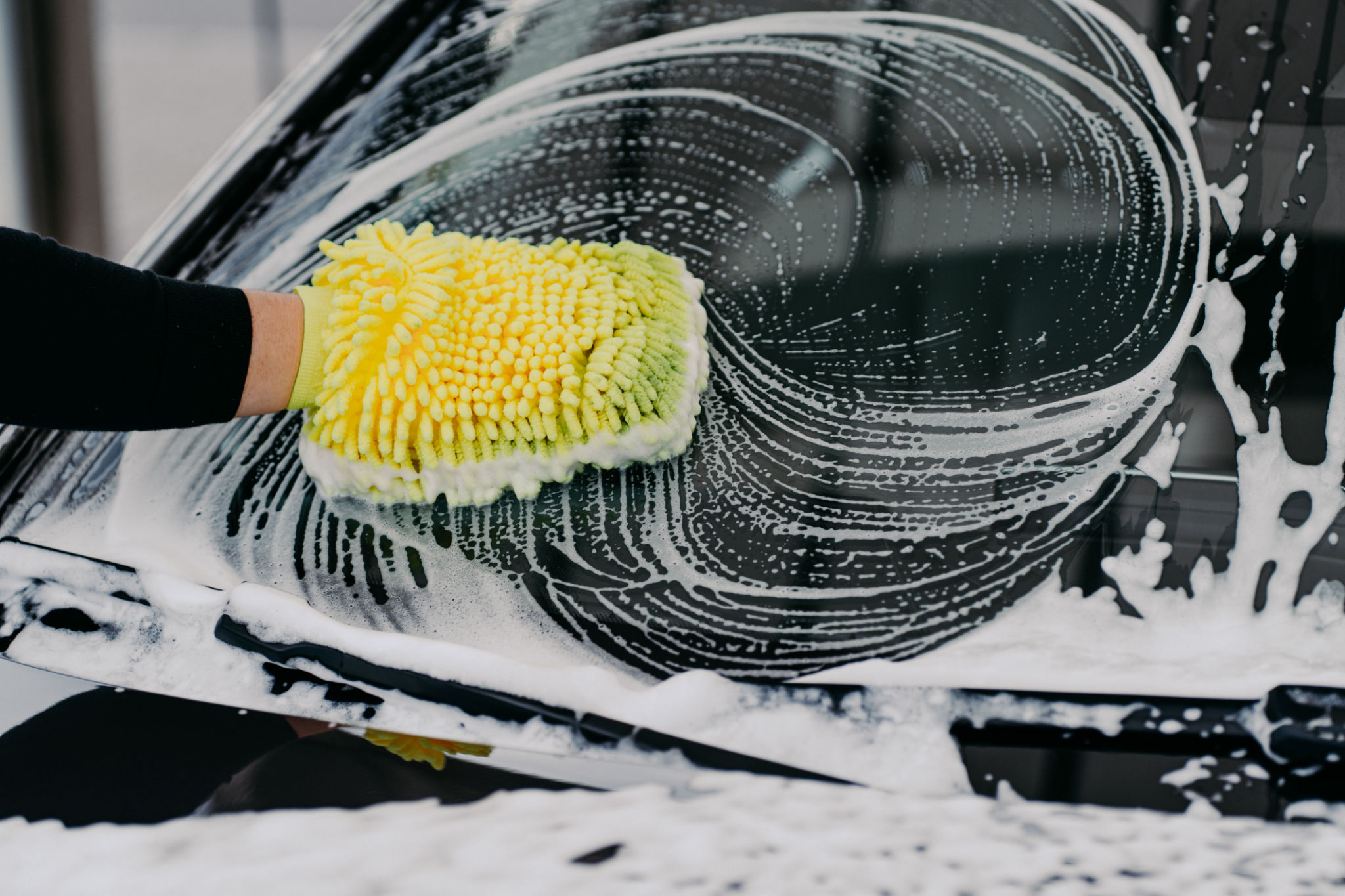 Car service concept. Unrecognizable man washes auto with cloth and car wash shampoo, has desire to cleanliness. Hand washing vehicle with sponge Car service concept. Unrecognizable man washes auto with cloth and car wash shampoo, has desire to cleanliness. Hand washing vehicle with sponge