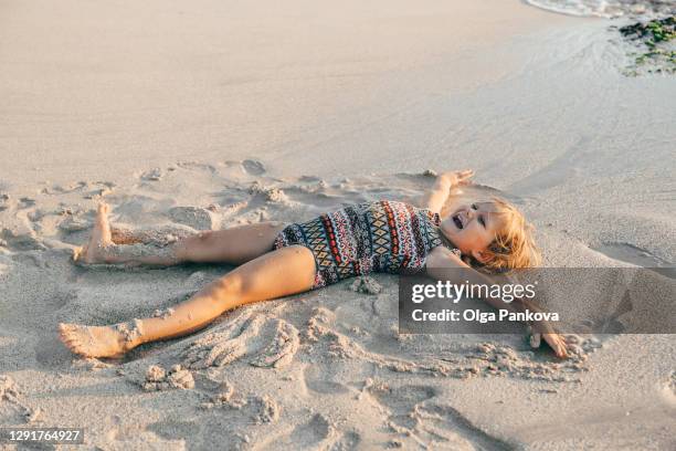 toddler girl having fun in the sand on the beach during sunset. playfully creating a sand angel. the indian ocean coast. bali island. beautiful view. family leisure. - heavenly resort stock pictures, royalty-free photos & images