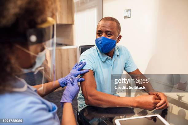 senior man receiving covid-19 vaccine from nurse at home - vaccine uk stock pictures, royalty-free photos & images