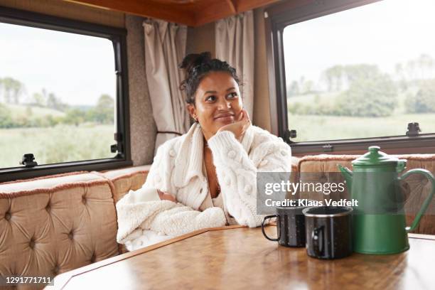 mother with hand on chin carrying baby daughter while sitting in camper van - family on couch with mugs stock-fotos und bilder