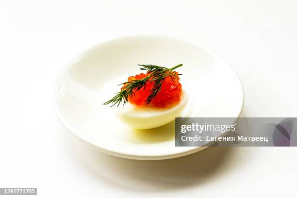 hard-boiled sliced chicken egg half with red caviar and dill on white plate background - canapé 個照片及圖片檔