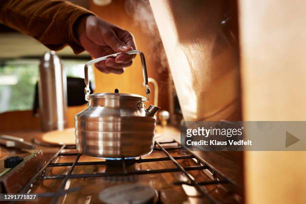 man's hand holding teakettle kept on burner in camper van - gas cooking stock-fotos und bilder