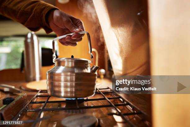 man's hand holding teakettle kept on burner in camper van - piano del fornello foto e immagini stock