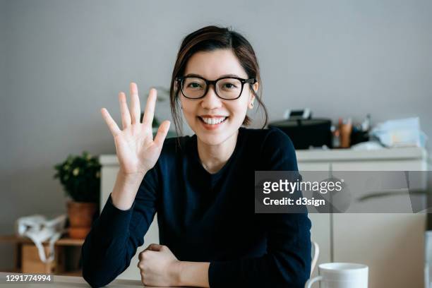 personal perspective of young asian woman working from home, waving hand and talking in front of the camera having video conference with her business partners on laptop at home - sventolare la mano foto e immagini stock