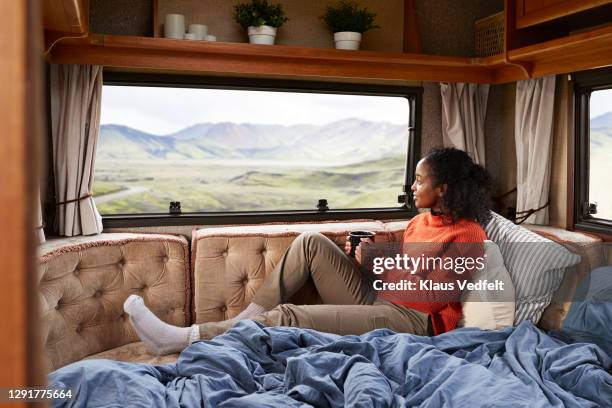 woman with coffee cup on bed in camper van - vehicle interior stock-fotos und bilder