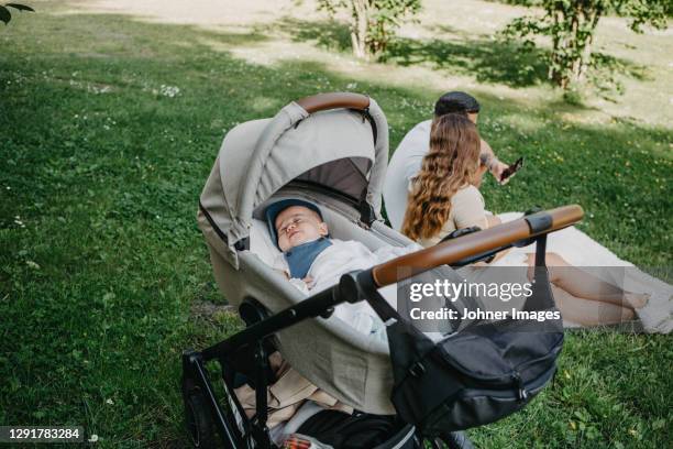 baby boy sleeping in pram, parents in background - baby bag stock-fotos und bilder