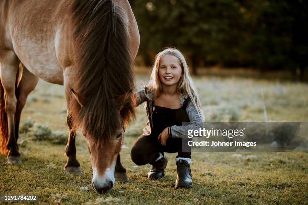 smiling girl crouching on meadow with grazing pony - provinz gotland stock-fotos und bilder