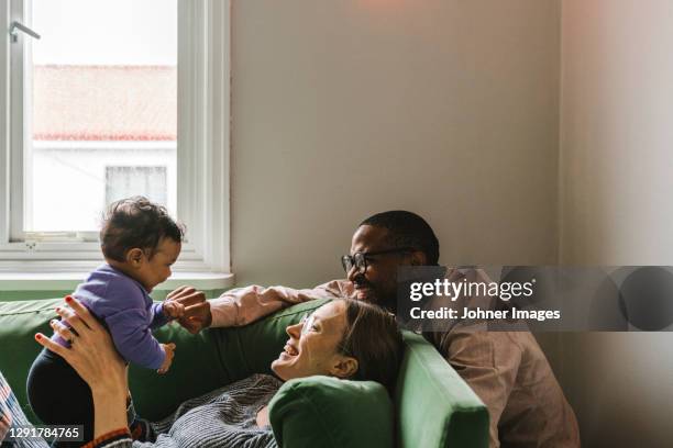 parents with baby girl sitting on sofa - parental leave stockfoto's en -beelden