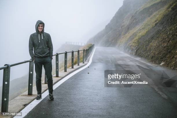 young man relaxes on foggy mountain road in the morning - hood clothing stock pictures, royalty-free photos & images