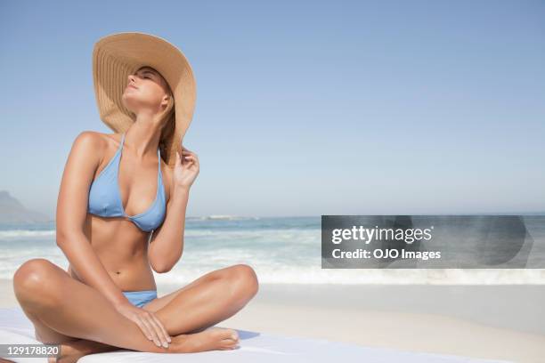 jeune femme en bikini assis sur la plage - chapeau de soleil photos et images de collection