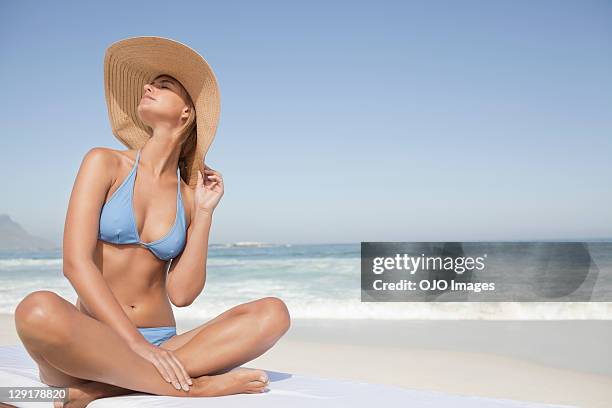 young woman in bikini sitting at beach - zonnehoed stockfoto's en -beelden