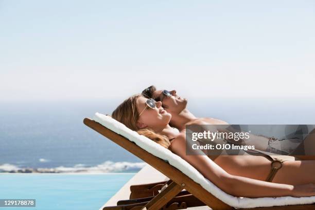 side view of couple resting on deck chairs near pool - sunbathing stock pictures, royalty-free photos & images