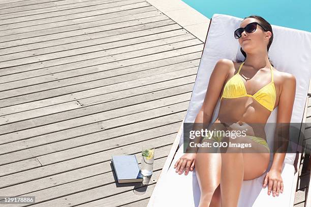 young woman resting on lounge chair at poolside - women sunbathing pool stock pictures, royalty-free photos & images