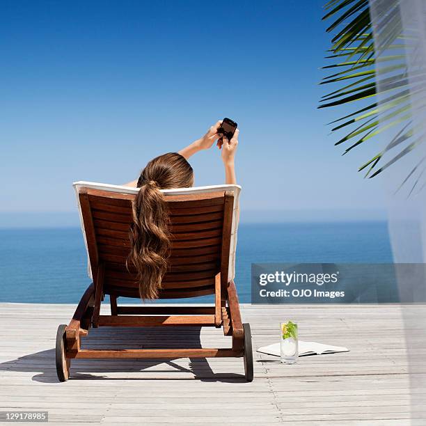 young woman holding mobile phone near pool - deckchair stock pictures, royalty-free photos & images