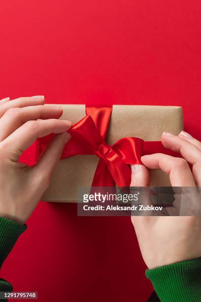 a girl in a green sweater is holding a beautiful box with a surprise tied with a bright ribbon on a red background. a woman opens gifts on her holiday. the concept of a happy christmas. - gift lounge stock-fotos und bilder