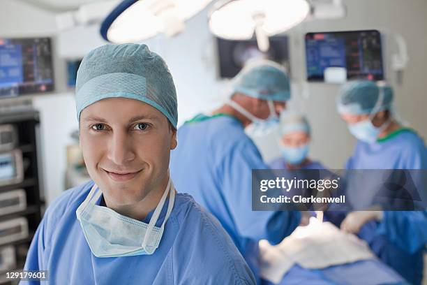 portrait of smiling young doctor in operating room - operating gown stock pictures, royalty-free photos & images