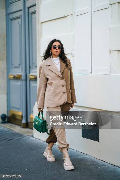 Gabriella Berdugo wears sunglasses, a white turtleneck pullover, earrings, a necklace, a bi color beige and brown oversized blazer jacket and suit...