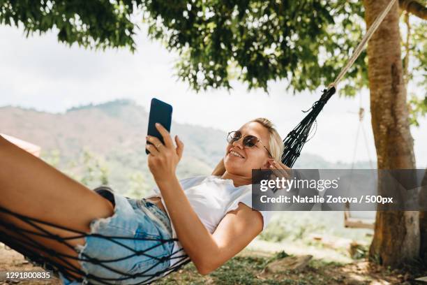 caucasian woman lying in hammock and using mobile phone while on vacation,khlong khian,thailand - woman smartphone nature stockfoto's en -beelden