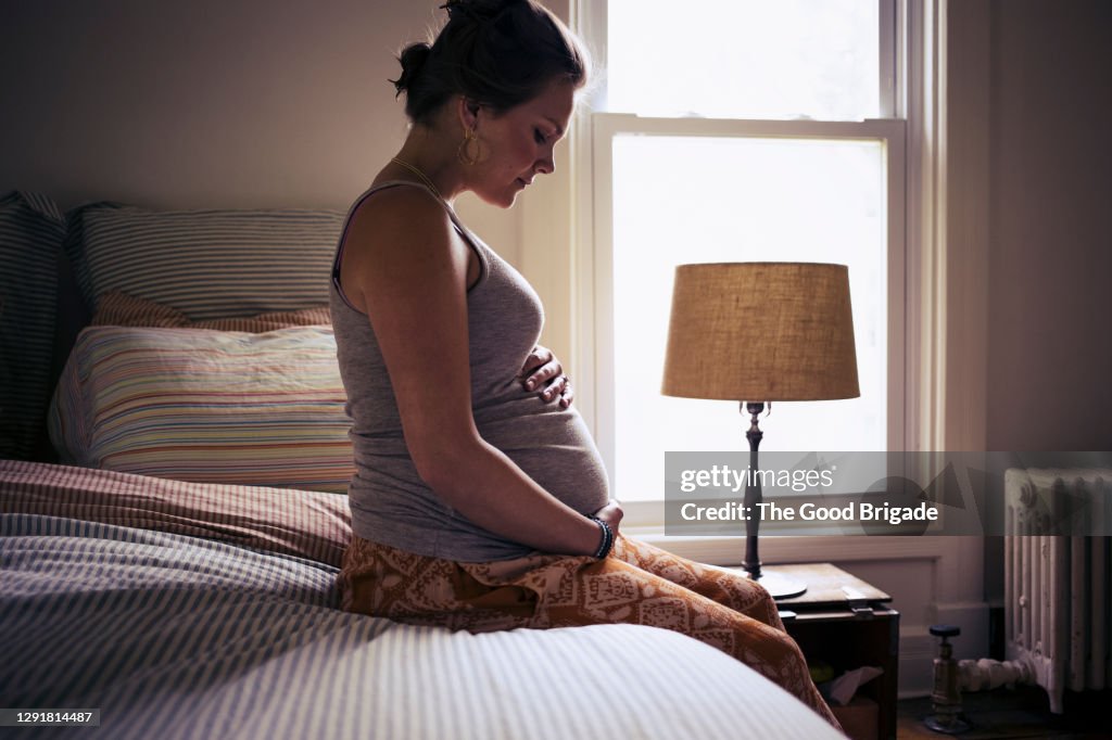 Pregnant young woman sitting on bed at home
