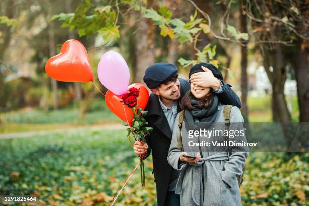 de jonge man verrassende vrouw met rozenboeket en de foto van de ballonnenvoorraad. datum / liefde / sint-valentijnsconcept. - saint valentin stockfoto's en -beelden