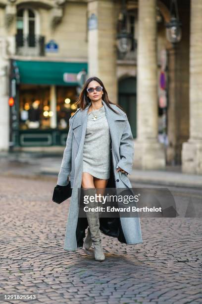 Patricia Gloria Contreras wears sunglasses, a gray long coat with large pockets from Balmain, a one-off-shoulder wool oversized long pullover worn as...