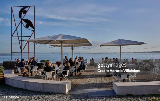 Patrons sit at tables of the Quiosque da Ribeira das Naus Bar during the COVID-19 Coronavirus pandemic on December 17, 2020 in Lisbon, Portugal. The...