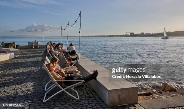 Patrons sit facing the river at lounge chairs of the Quiosque da Ribeira das Naus Bar during the COVID-19 Coronavirus pandemic on December 17, 2020...