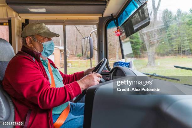 senior man, the bus driver wearing the protective surgical mask, driving a school bus during the covid-19 pandemic bin the rural area. - alex potemkin coronavirus stock pictures, royalty-free photos & images