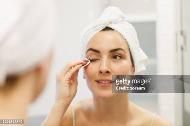 woman's reflection in the bathroom mirror, wearing towel on head and removing eye make-up - rubbing stock pictures, royalty-free photos & images