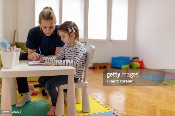 female tutor assisting girl in graphomotor exercise - child care worker stock pictures, royalty-free photos & images